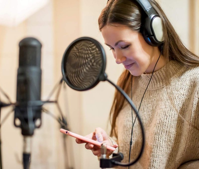Female voiceover artist recording audio in professional studio with microphone